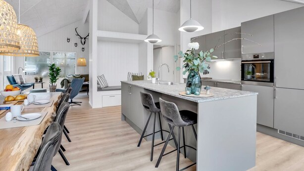 A modern kitchen with a central island, bar stools, and a dining area with a wooden table and chairs.