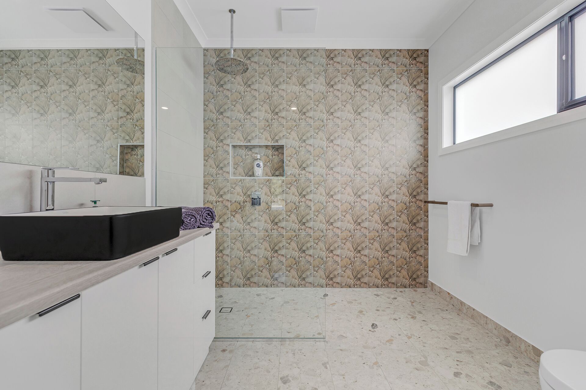 Un bany modern amb un mirall gran, un lavabo negre, una dutxa amb porta de vidre i un vàter.