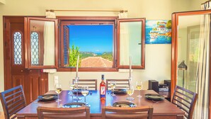 Une table à manger dressée avec des verres à vin, des assiettes et une bouteille, offrant une vue pittoresque par la fenêtre.