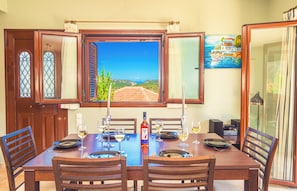 Mesa de jantar posta com copos de vinho, pratos e uma garrafa, com vista panorâmica pela janela.
