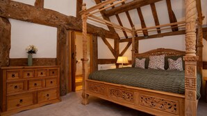 Una cama tradicional de madera con dosel y detalles tallados, un aparador de madera con cajones y una puerta con marco de madera.