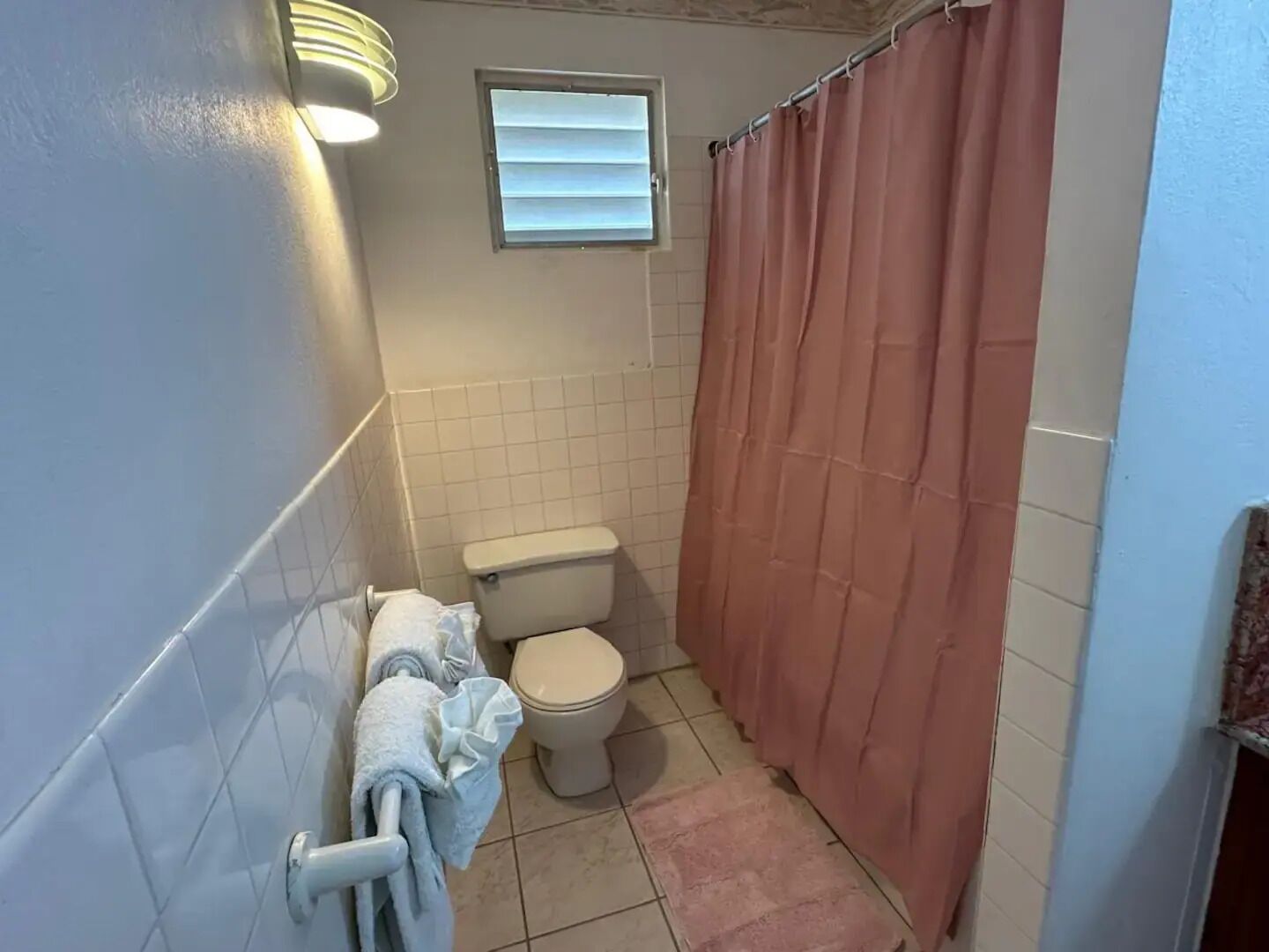 Un baño pequeño con inodoro, toallero con toallas, cortina de ducha y ventana con persianas.
