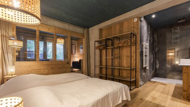 A bedroom with a large bed, wooden wardrobe, and a bathroom with a shower. - Loft Bellevue Remonté | Centre | Piscine | Parking (Les Houches)