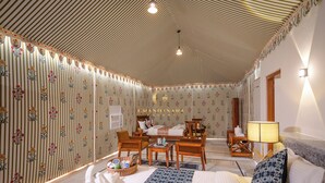 Ein Hotelzimmer mit gestreiftem Deckenpaneel, floraler Tapete, einem Bett mit blumigem Überwurf, Holzmöbeln und einer Lampe.