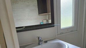 A bathroom with a white sink, dark wood cabinets, a glass shelf above the sink, and a window with a view of the outside. - Gite in the heart of nature 15 minutes from Colmar  (Widensolen)