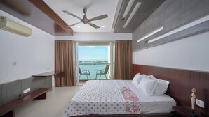 A hotel room with a bed, a desk, a chair, and a balcony with a view. - Spacious 3-bedroom water front apartment in serene Marine Drive Ernakulam Kerala (ERNAKULAM)