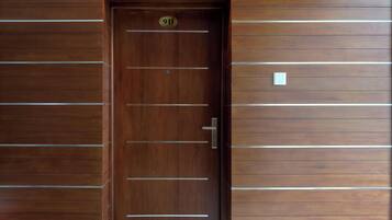 Una puerta de madera con una placa de número, una lámpara arriba y un felpudo con diseño floral.