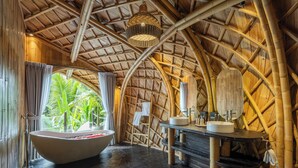 A bamboo-themed bathroom with a large bathtub, a vanity with a mirror, and a view of lush greenery.