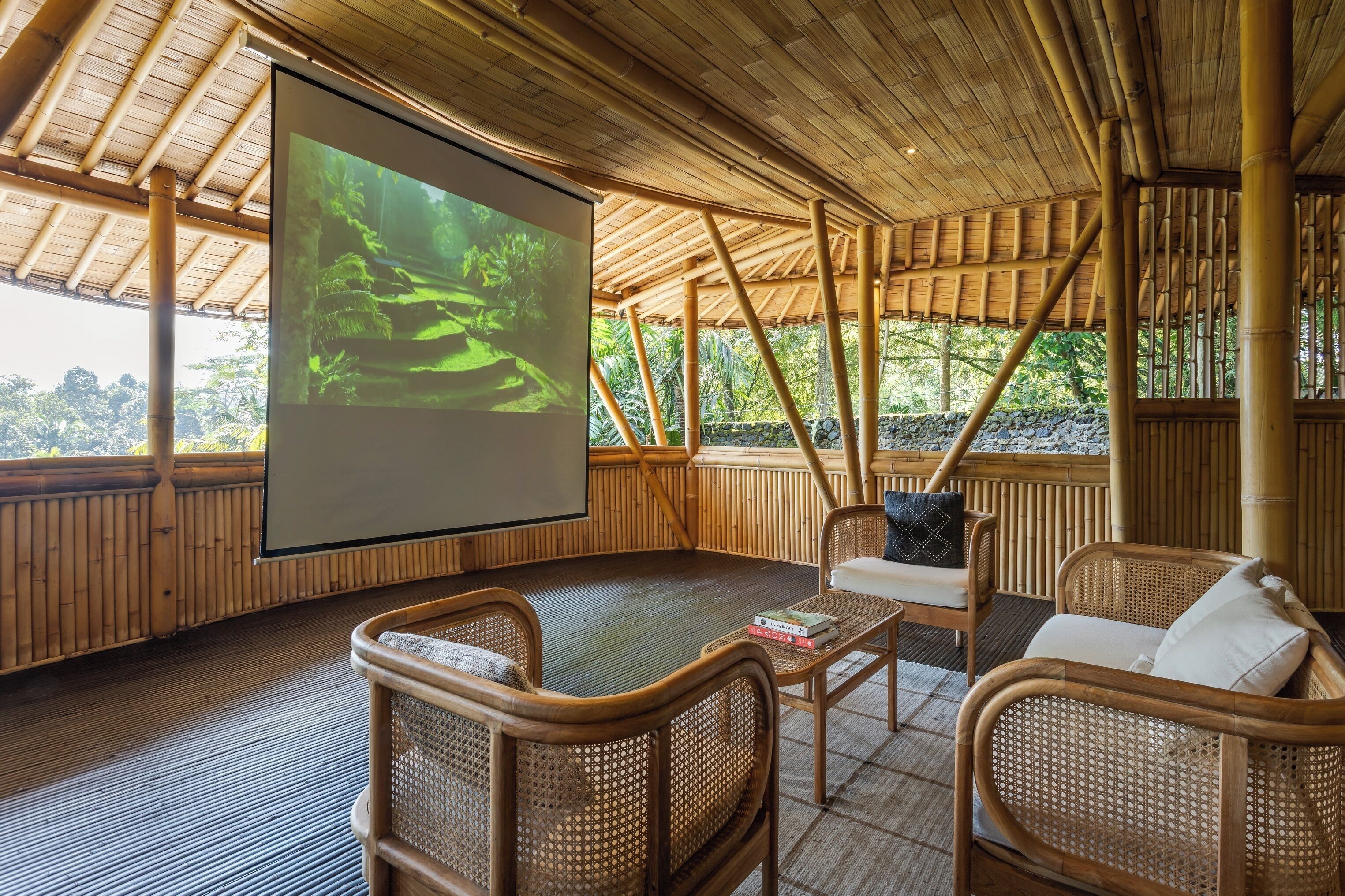 A bamboo-paneled room with a large screen, wicker furniture, and a view of lush greenery.