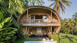 A large, round, wooden house with a balcony, surrounded by lush greenery and a swimming pool.