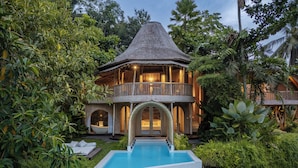 A two-story house with a pool, surrounded by lush greenery.