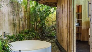 A spa area with a stone pathway leading to a circular hot tub, surrounded by lush greenery and bamboo structures.