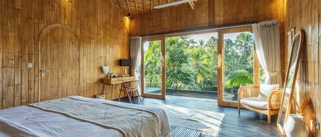 A room with a bed, a desk, a chair, and a large window with a view of greenery.