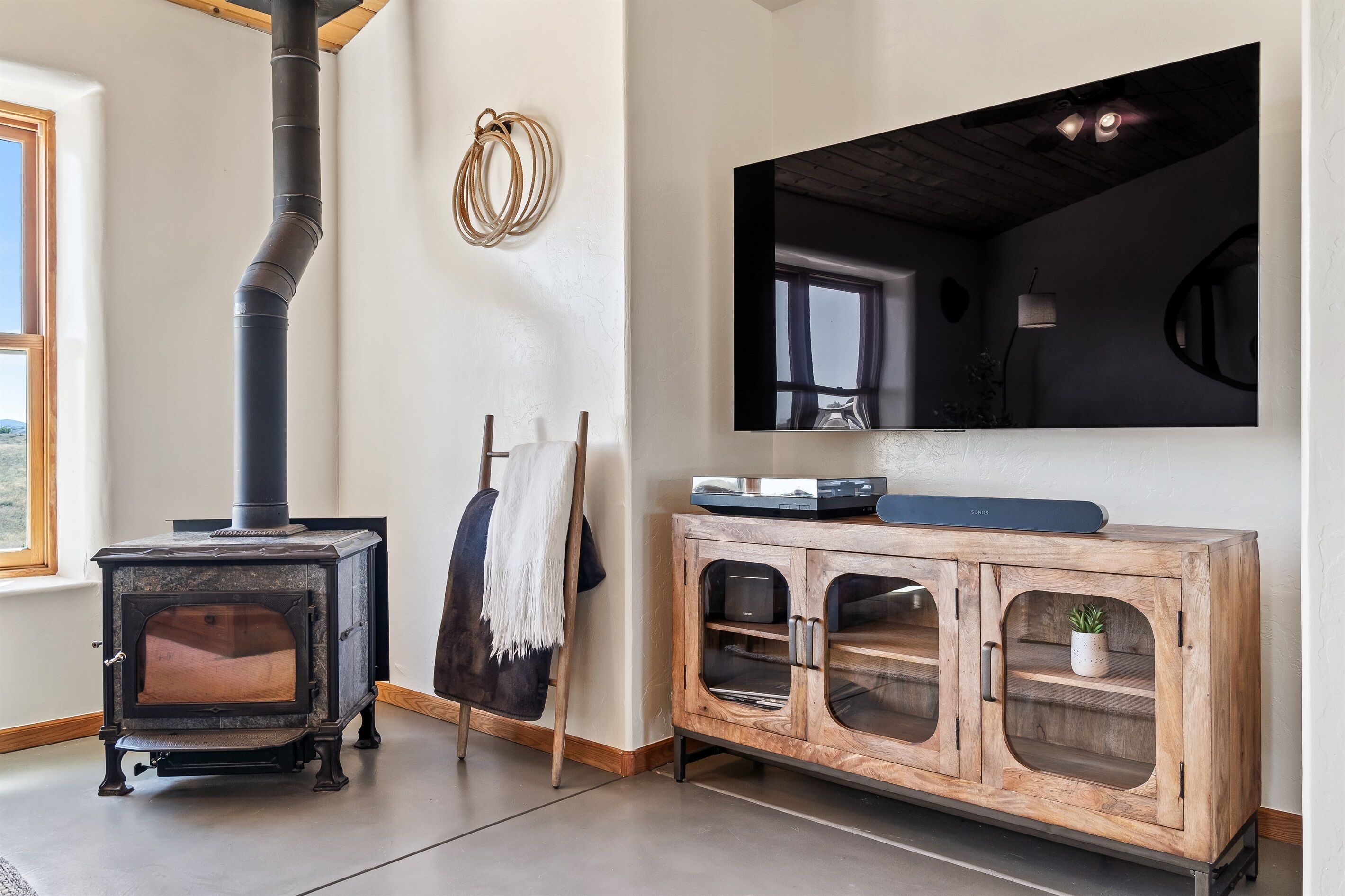 Una habitación con estufa de leña, un mueble de madera con puertas de cristal y un espejo grande en la pared.