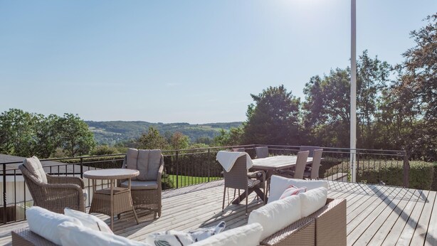 Eine Holzterrasse mit Korbmöbeln und einem Tisch, mit Blick auf eine reizvolle Landschaft.