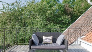 Ein Balkon mit einem Korbssessel, Kissen und einem Glastisch.