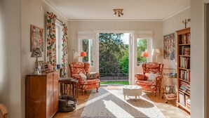 Ein geräumiges Wohnzimmer mit einem großen Fenster, zwei Sesseln, einem Sofa, einem Holzschrank und einem Bücherregal.