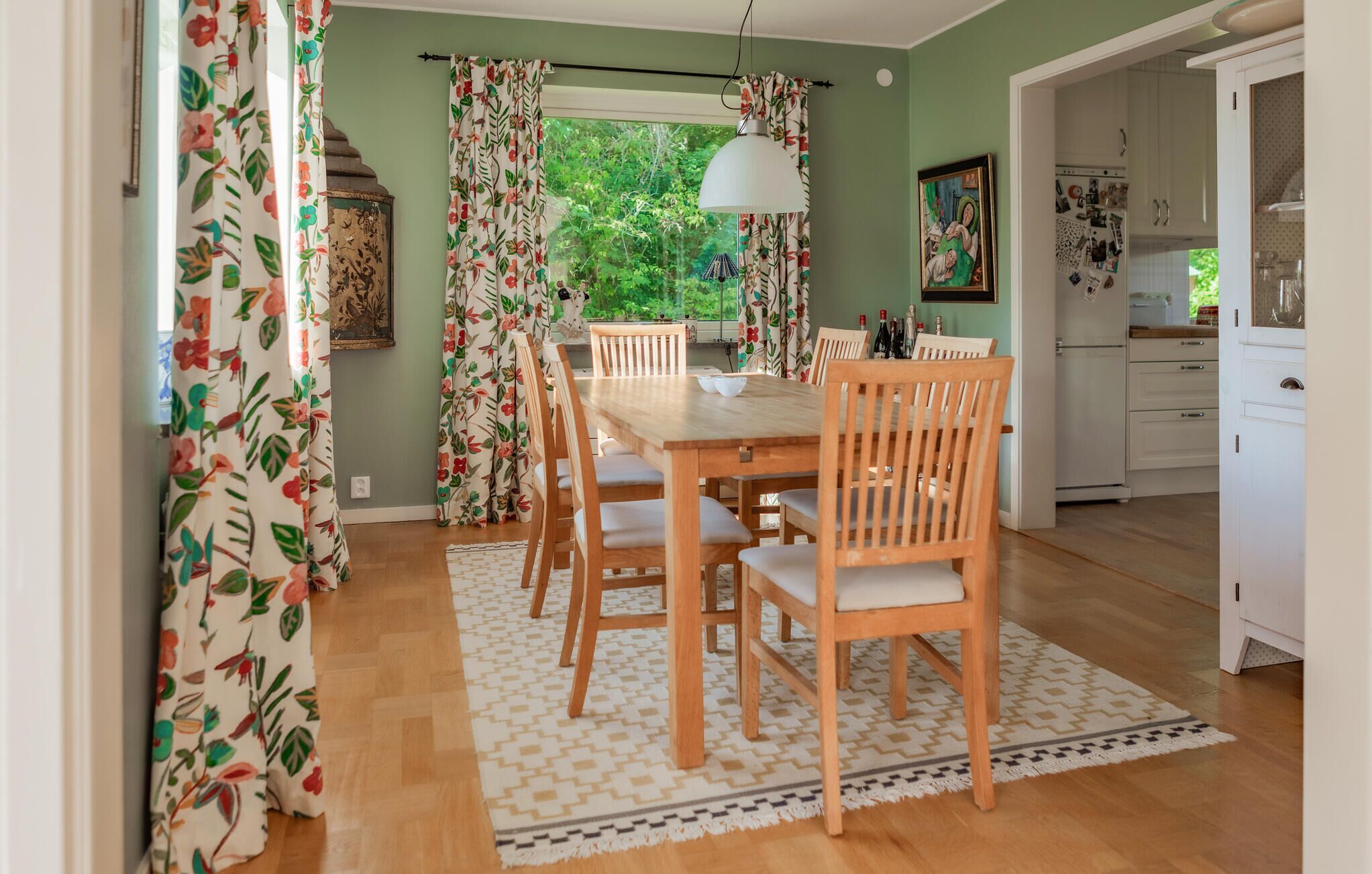 Un espace repas avec une table et des chaises en bois, un tapis à motifs et une vue sur l’extérieur.