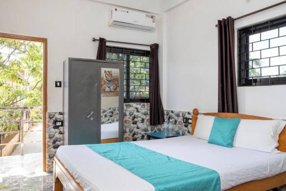 A bedroom with a bed, a wardrobe, a window with curtains, and an air conditioning unit.