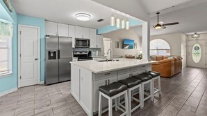 Una cocina moderna con armarios blancos, electrodomésticos de acero inoxidable y una isla central con taburetes de bar.
