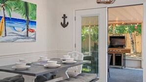 Un comedor con una mesa dispuesta para cuatro personas, un cuadro de una playa y un cartel que dice 'the BEACH'.
