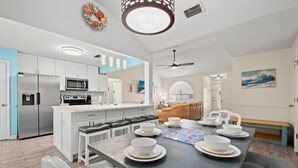 Una cocina moderna con armarios blancos, una isla central y un comedor con una mesa grande para cuatro.