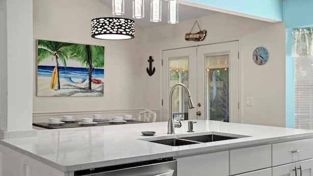 Una cocina moderna con encimera blanca, electrodomésticos de acero inoxidable y un cuadro de una playa.