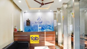 A hotel reception area with a reception desk, a sofa, and a ceiling fan. - Fabhotel Prime Culture (Noida)