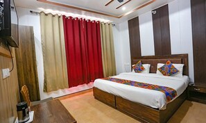 A hotel room with a wooden bed, red curtains, and a small table with a kettle. - Fabhotel Maya (Dehradun)