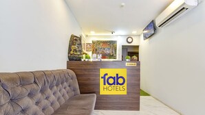 A reception area with a tufted sofa, a wooden reception desk, a 'fab hotels' sign, a clock, and a TV mounted on the wall. - Fabhotel Rush Imperial (Indore)