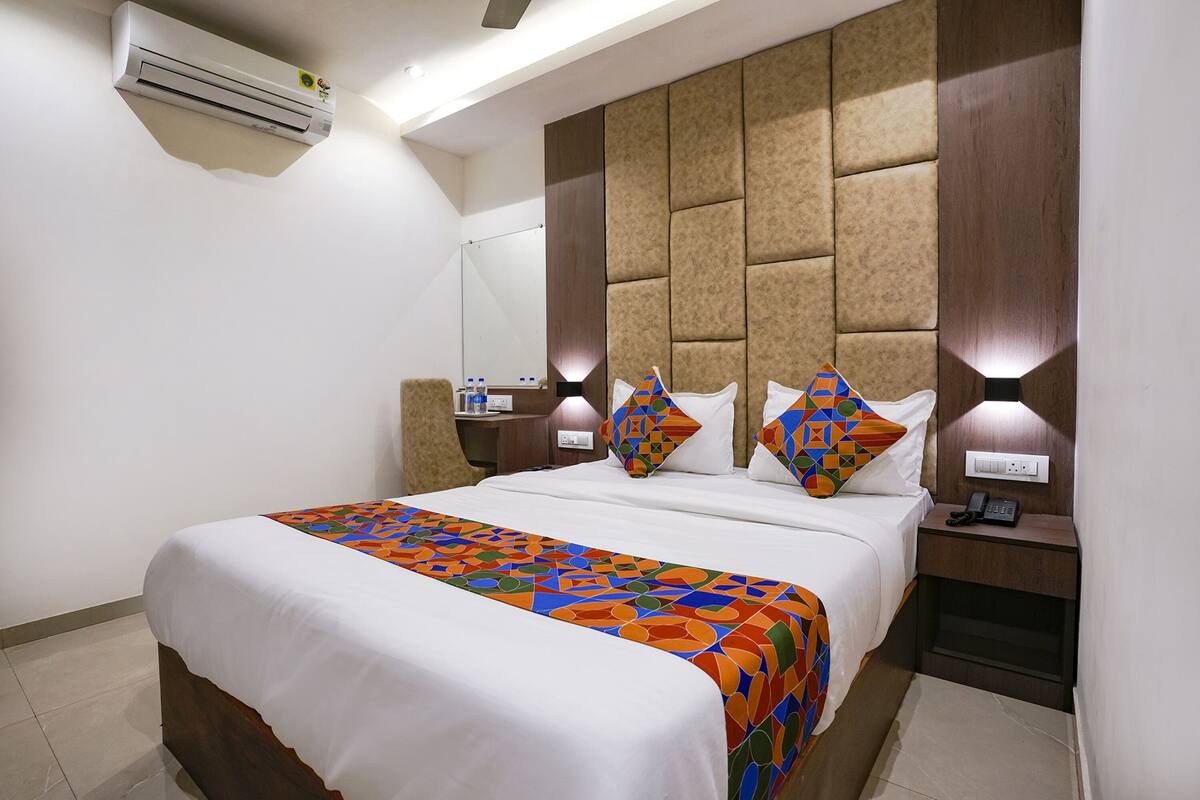 A hotel room with a large bed, a headboard with a geometric pattern, bedside lamps, a nightstand, and an air conditioning unit.