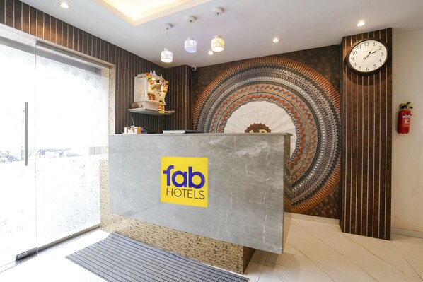Un espace d’accueil d’hôtel au design moderne, comprenant un comptoir d’accueil, un mur décoratif orné de motifs géométriques et une horloge.