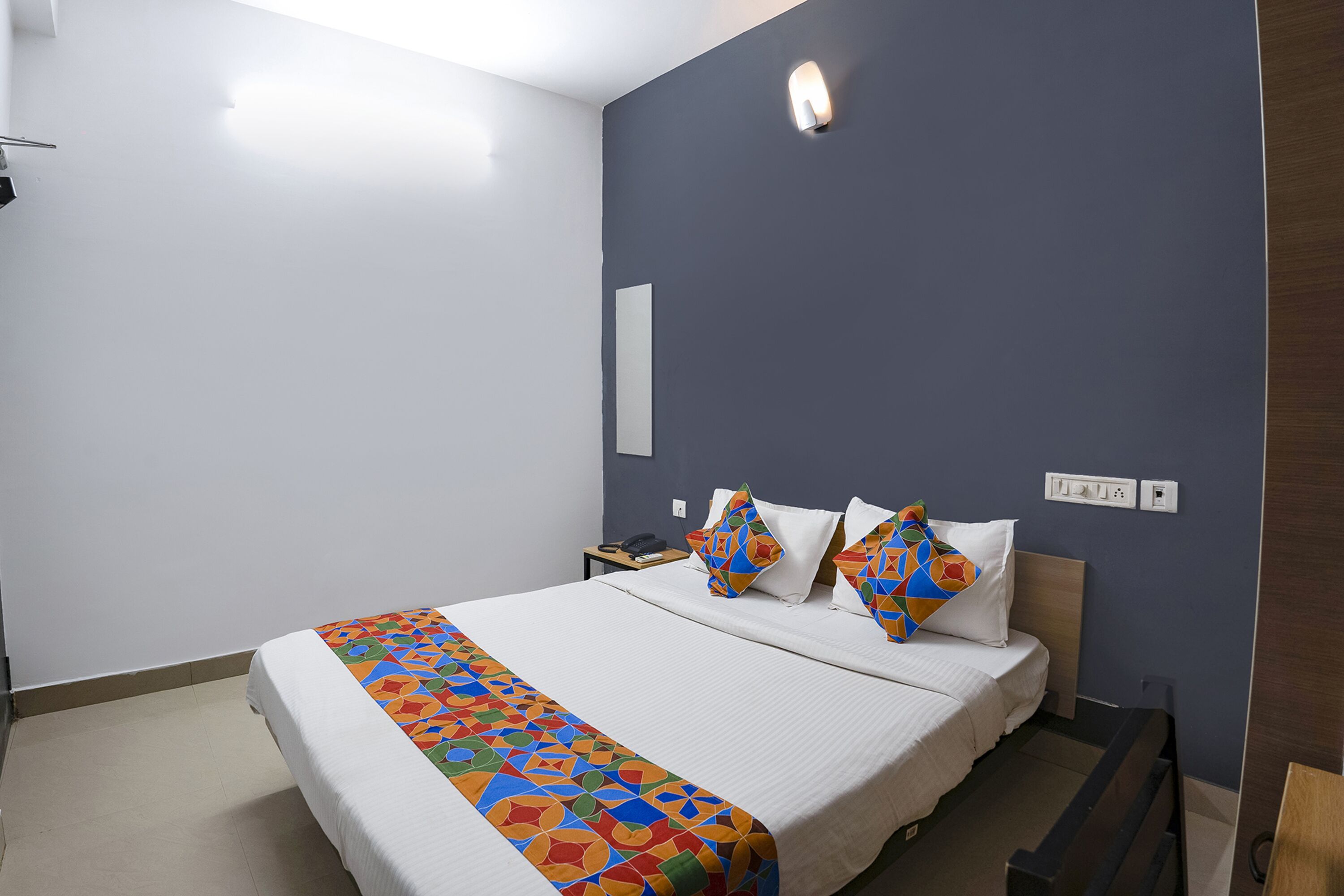 A hotel room with a large bed, a bedside table, a nightstand, and a wall-mounted light.