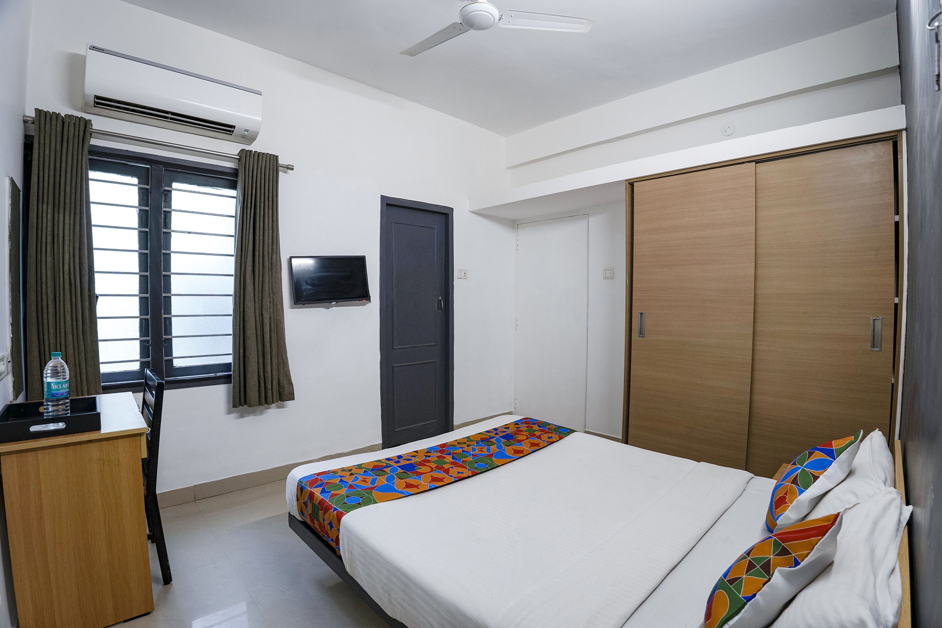 A hotel room with a bed, a desk, an air conditioner, a wardrobe, and a television on the wall.