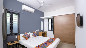 A bedroom with a bed, a bedside table, a wardrobe, a ceiling fan, and an air conditioning unit. - Fabhotel Bella Vagues (Tirupporur)