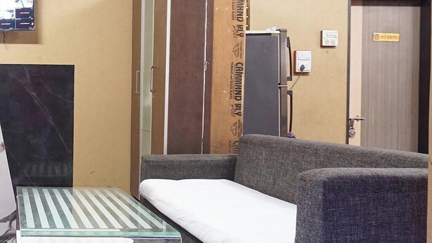 A room with a sofa, a small table, a refrigerator, and a door with a sign. - Fabhotel Shree Haree Residency (Pune)