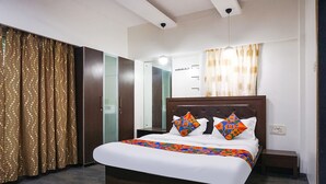 A bedroom with a large bed, a wardrobe, a bedside table, and a hanging light fixture. - Fabhotel Shree Haree Residency (Pune)