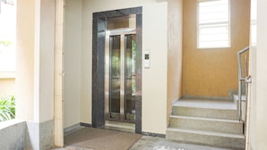 A hotel entrance with a glass elevator, a set of stairs, and a door with a handle. - Fabhotel Shree Haree Residency (Pune)