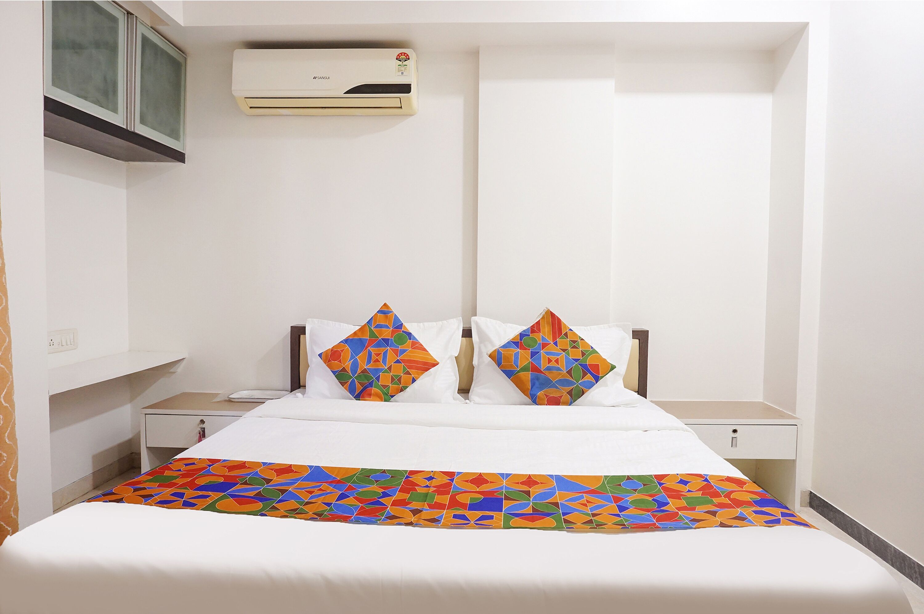 Une chambre d’hôtel avec un lit, deux tables de chevet, un appareil de climatisation et une fenêtre donnant sur un paysage agréable.