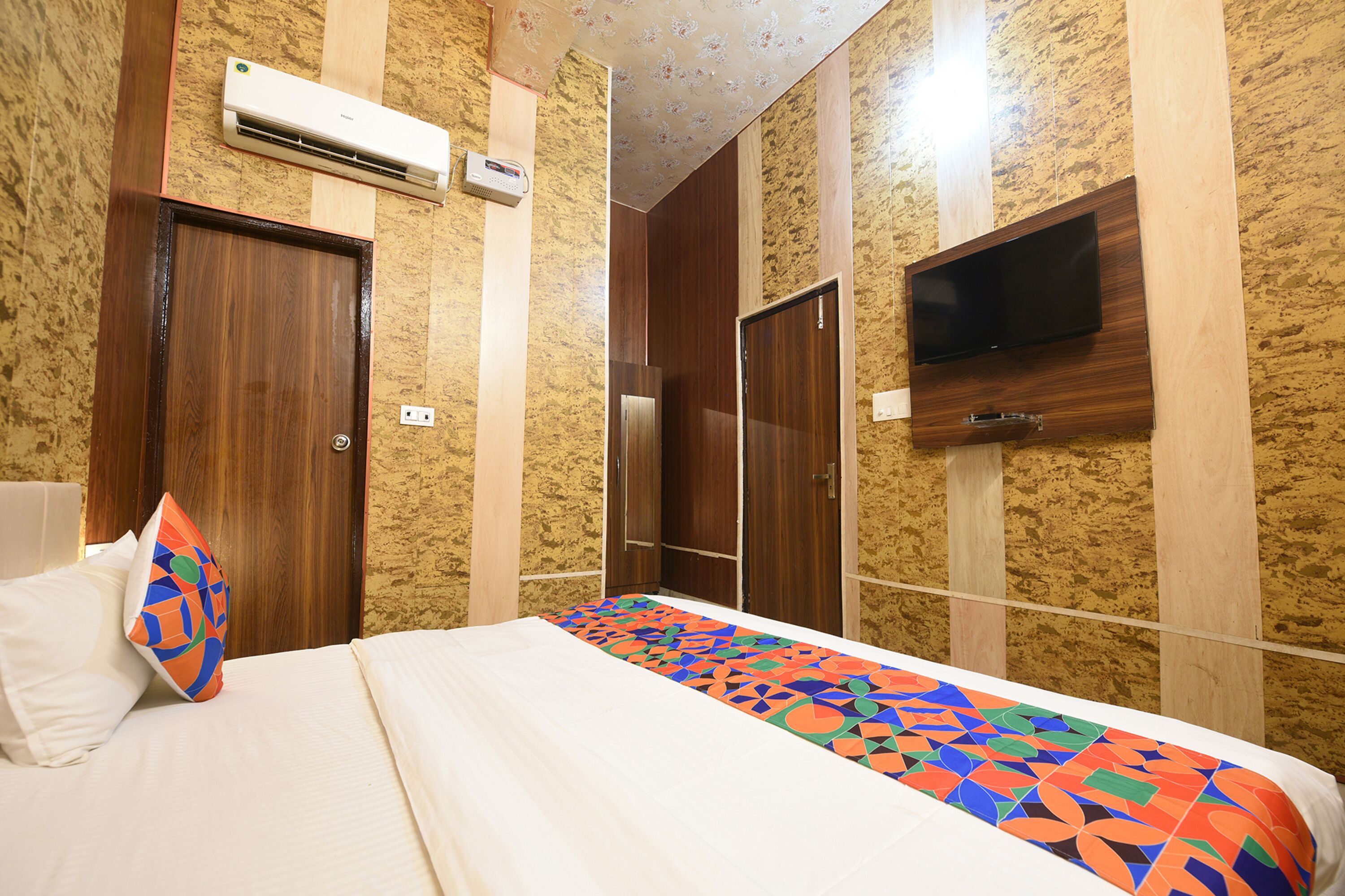 Une chambre d’hôtel avec un lit, un téléviseur fixé au mur et un appareil de climatisation placé au-dessus du lit.