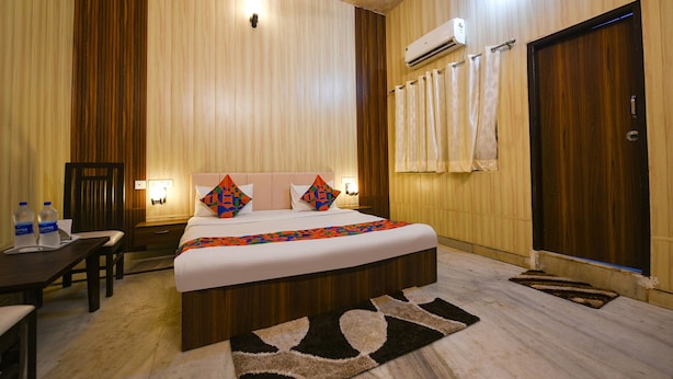Ein Hotelzimmer mit einem großen Bett, einem Schreibtisch und einem Sessel. An der Wand befindet sich eine Klimaanlage und eine Tür mit Vorhängen.