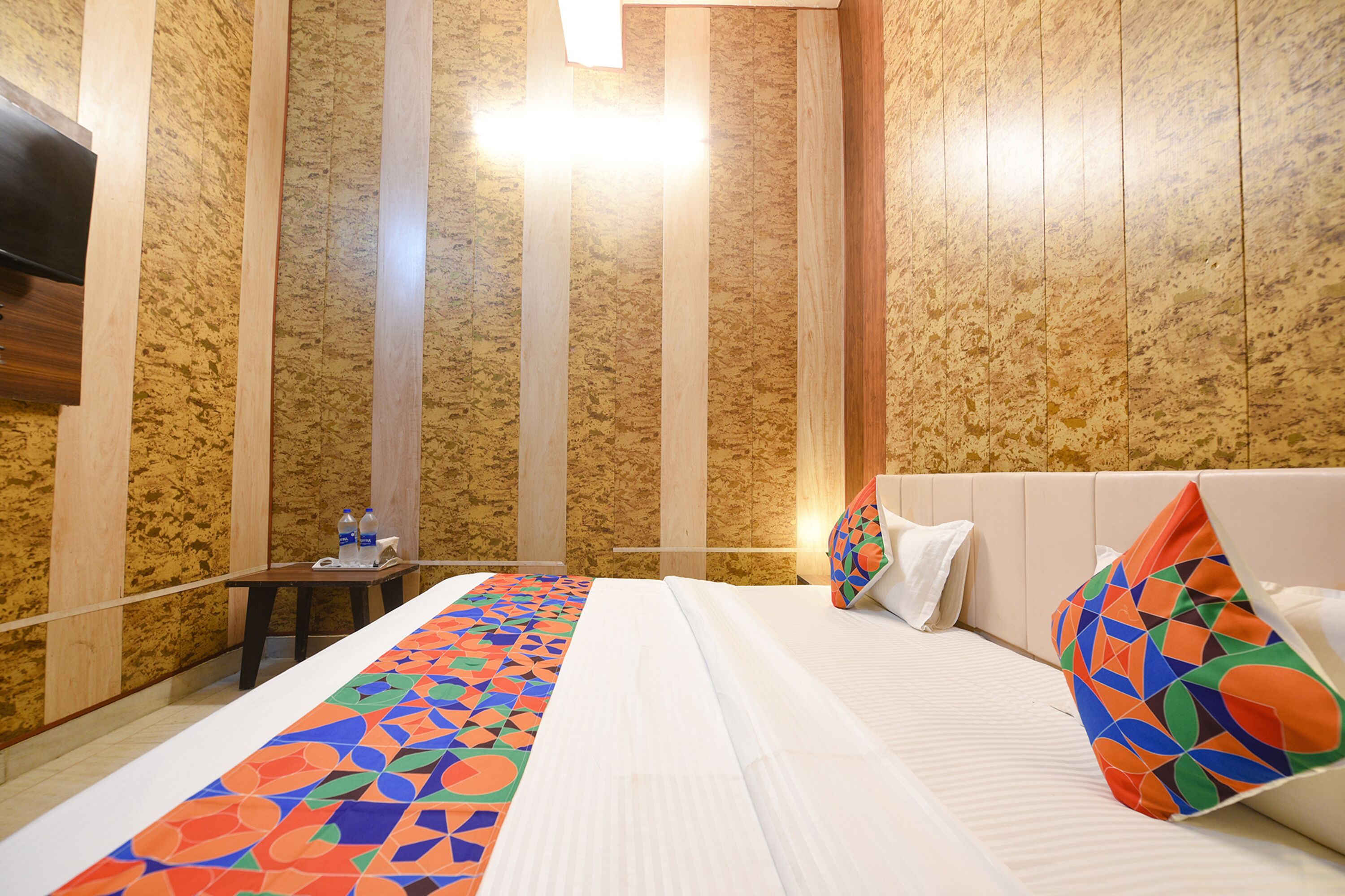 A hotel room with a bed, a bedside table with water bottles, and a patterned bed runner.