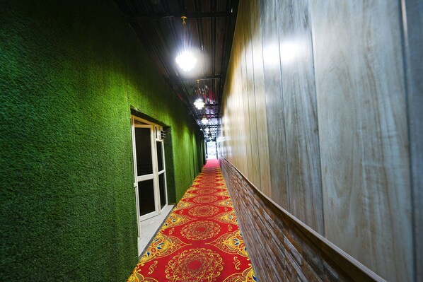 A hallway with a red carpet, green walls, and a wooden panel on one side. - Via Grand Palace (Faridabad)