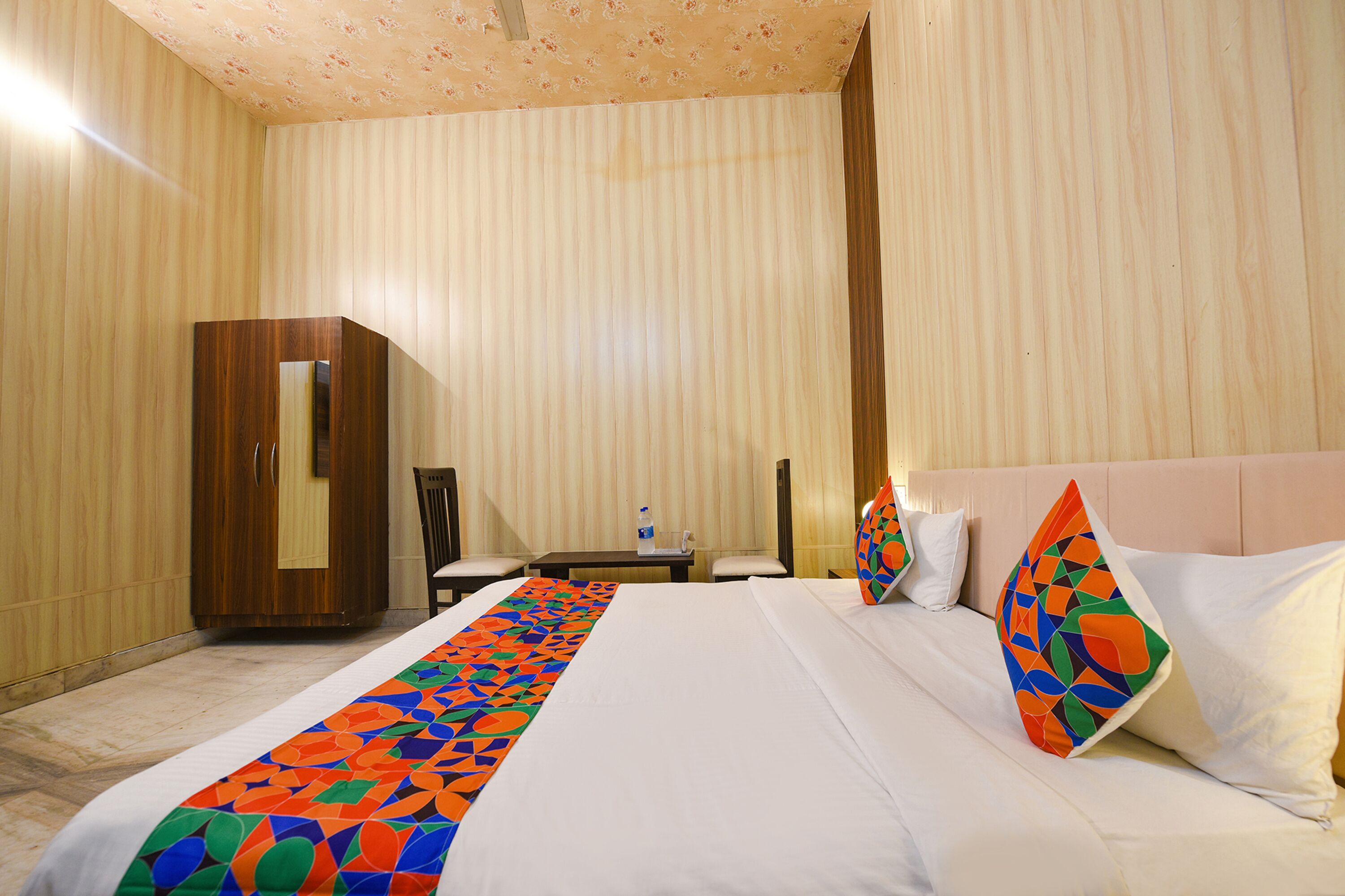 A hotel room with a bed, a wooden wardrobe, a desk with a chair, and a nightstand.