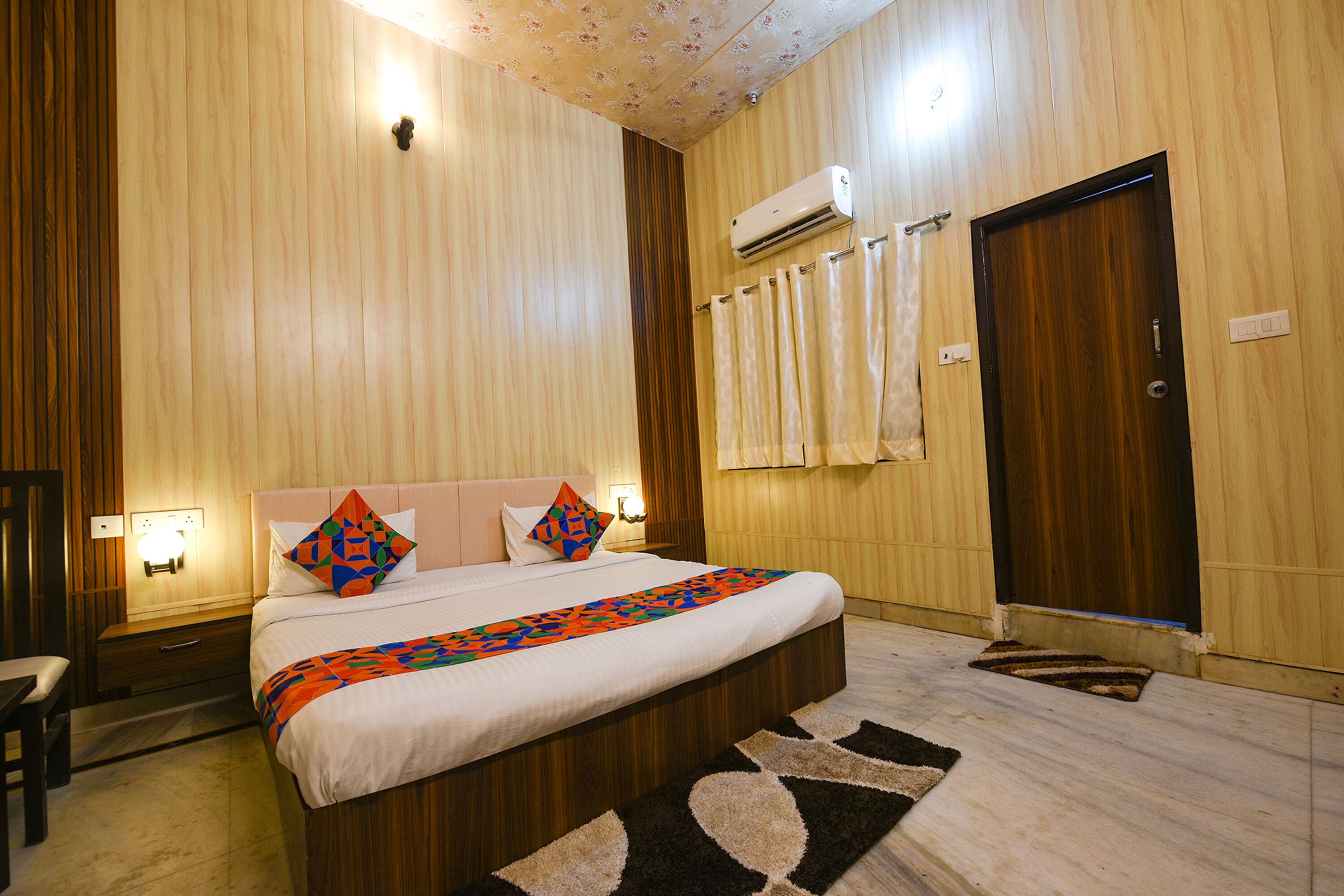 Habitación de hotel con una cama grande, paneles de madera en las paredes, un equipo de aire acondicionado, una mesita de noche y un escritorio.