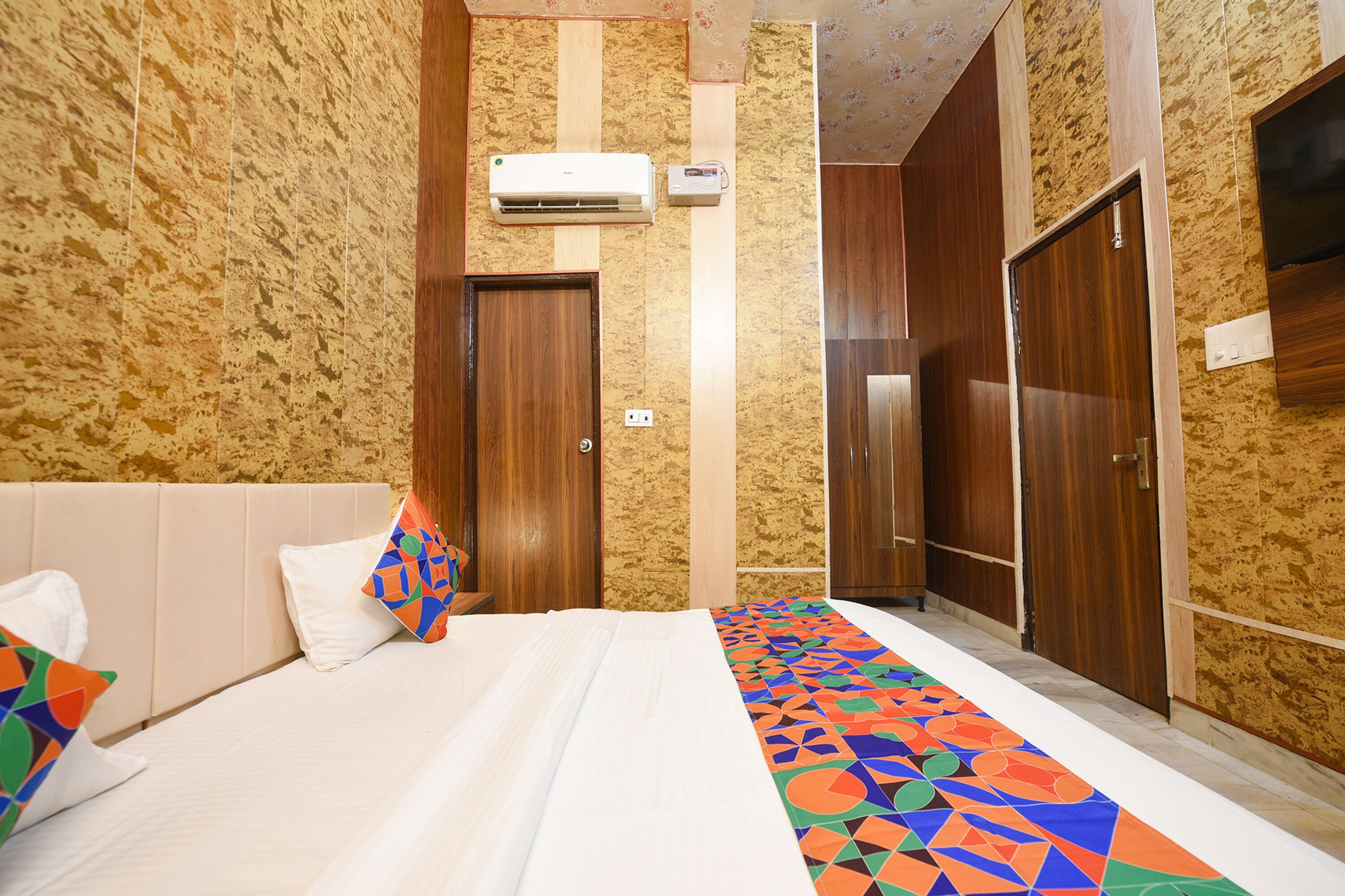 A hotel room with a bed, a wooden wardrobe, and an air conditioning unit.