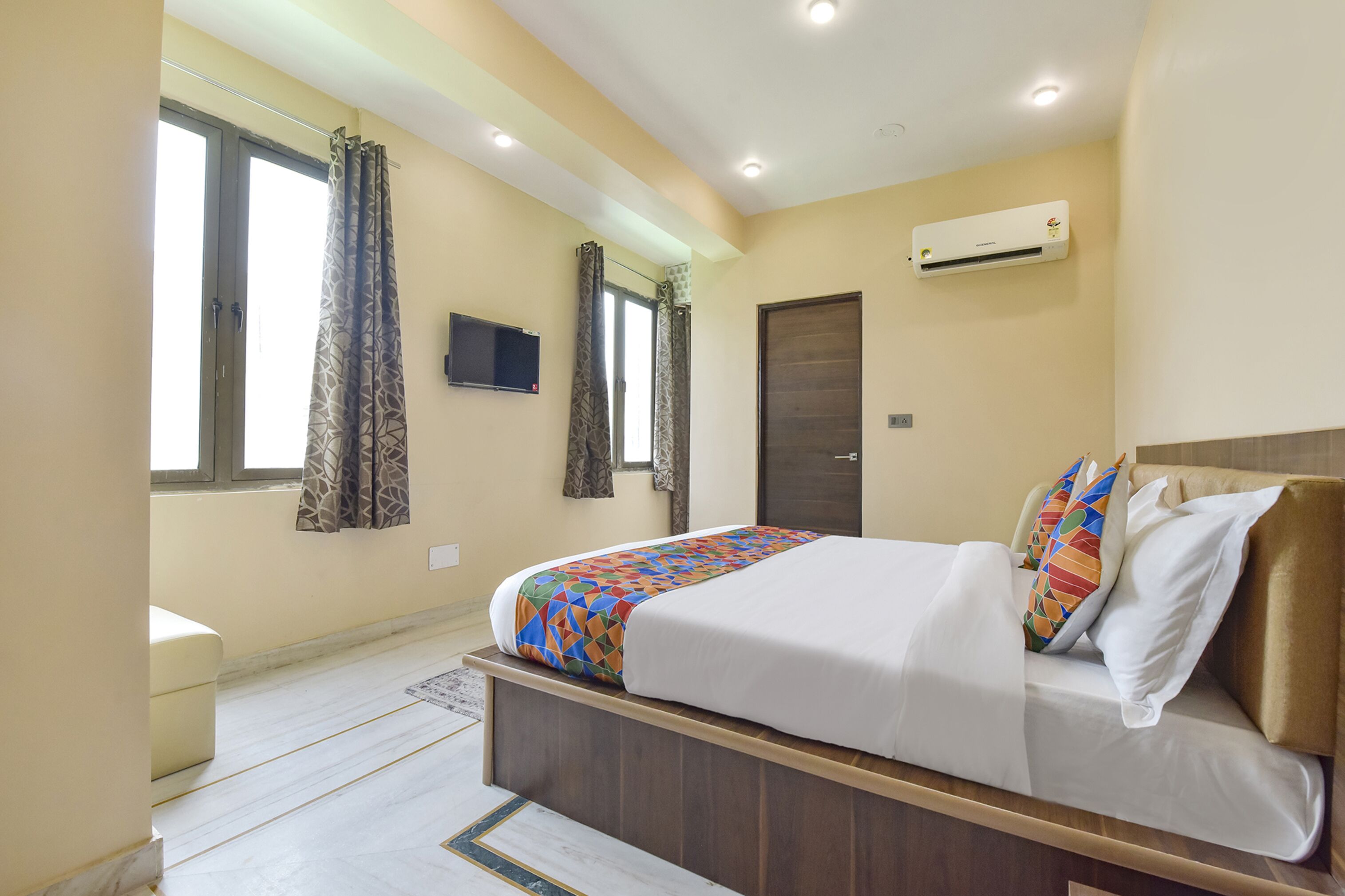 A bedroom with a bed, curtains, a TV, an air conditioner, and a door.