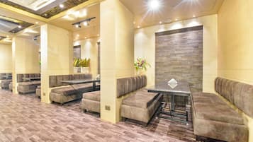 A modern lounge area with cushioned seating, a central table, and a decorative wall.