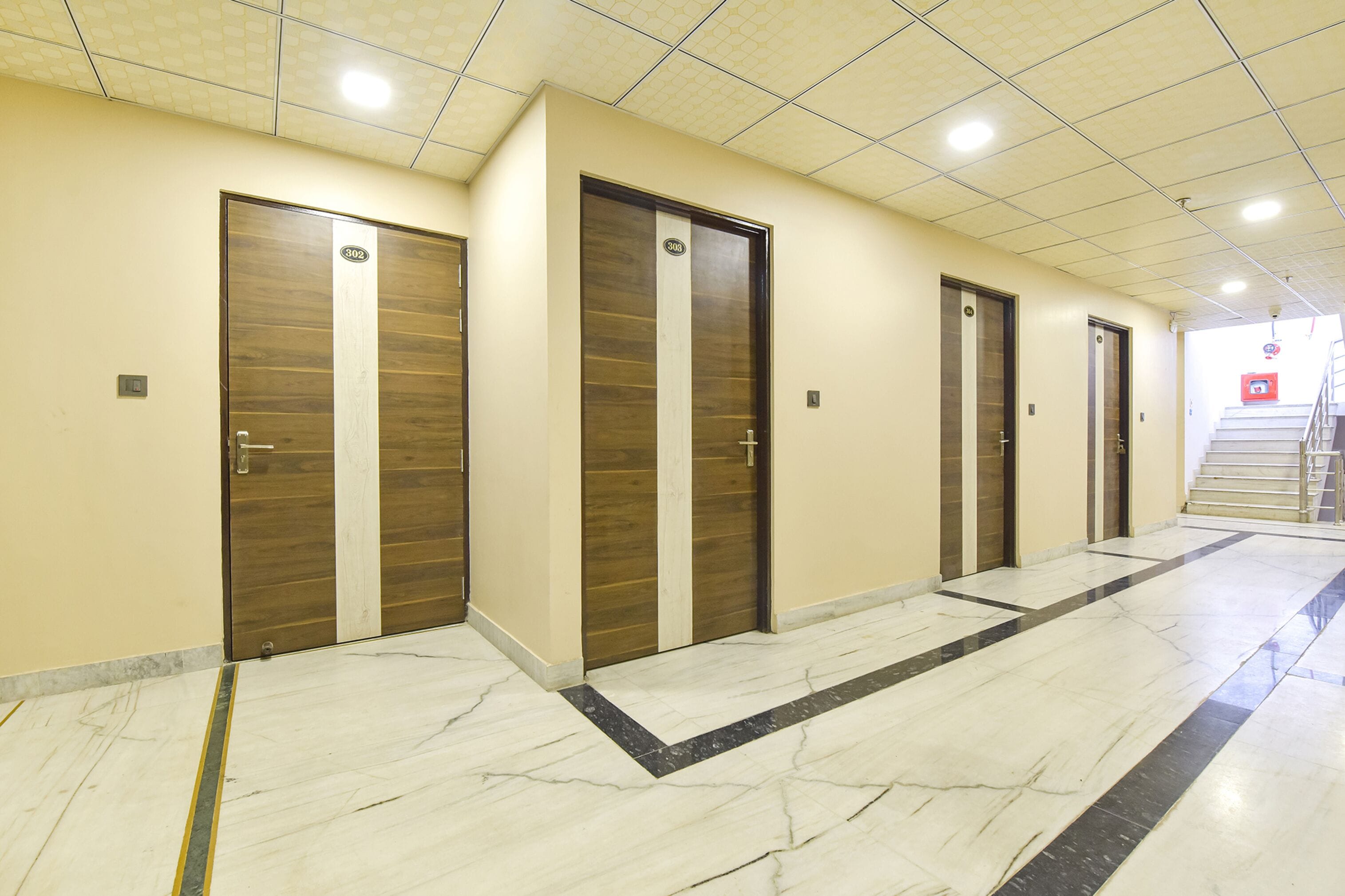 A hallway with four wooden doors, each marked with a number. The floor is tiled with a marble pattern.