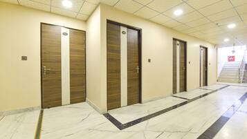 A hallway with four wooden doors, each marked with a number. The floor is tiled with a marble pattern.